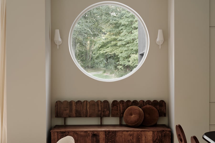A circle window gives a view of greenery outside while a wooden bench provides seating below.