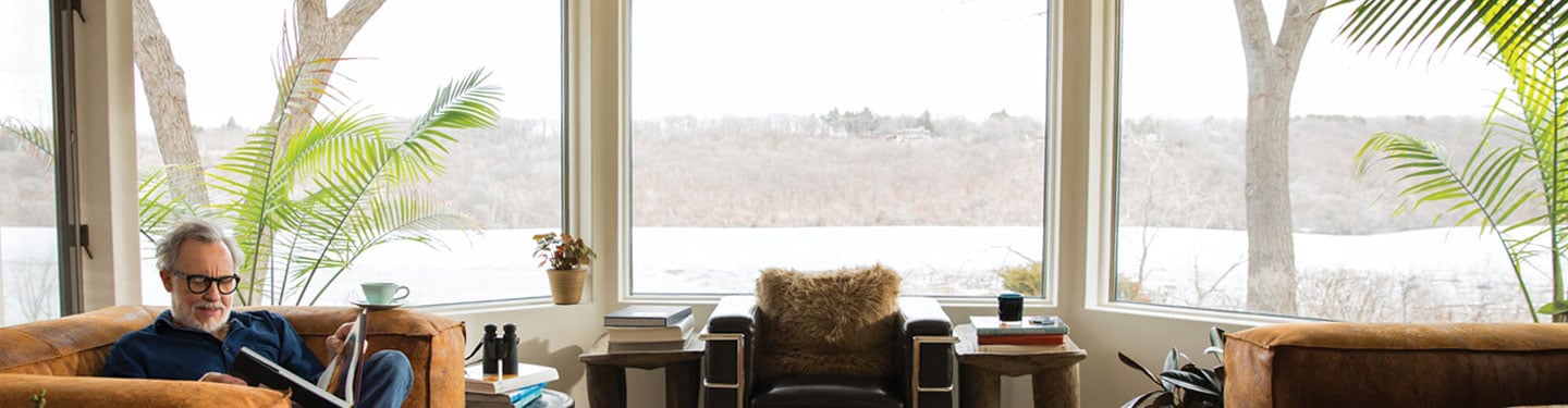 Man reading a book in his living room with Andersen 400 series casement & picture types of windows