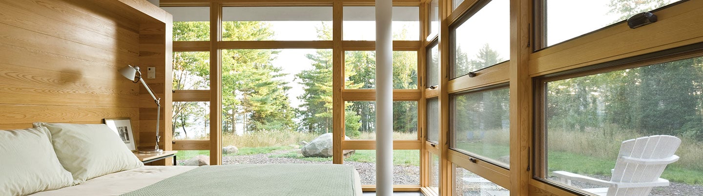 Bedroom with wall to wall awning windows set in forest