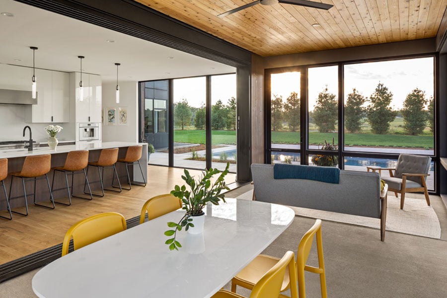 A porch and kitchen with floor-to-ceiling windows facing a backyard swimming pool and row of trees.
