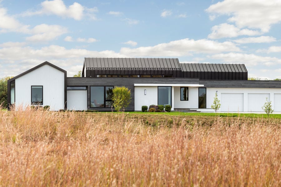 A contemporary prairie home with a unique look featuring a combination of siding types including black standing-seam metal, white polyash, and a thermally treated wood.