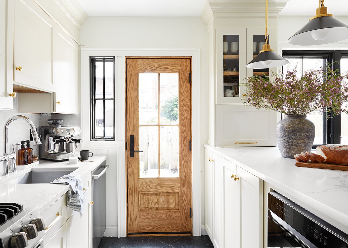 A remodeled kitchen with creamy white cabinetry, a white oak Andersen entry door and black A-Series windows.