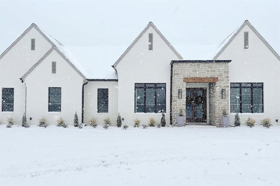 A white home with new black windows is snug against the snowy, cold landscape outside. 
