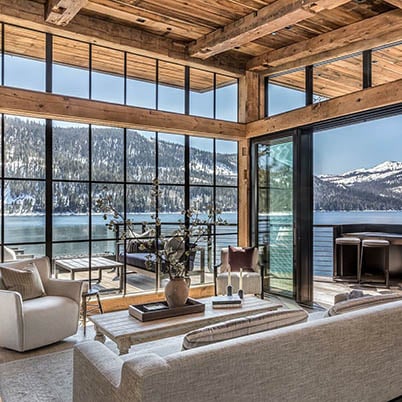 House with wooden interior and large black windows overlooking a lake and mountains
