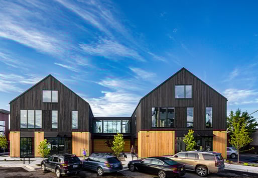 A street view of a mixed-use building with two parallel volumes connected via a skyway. 