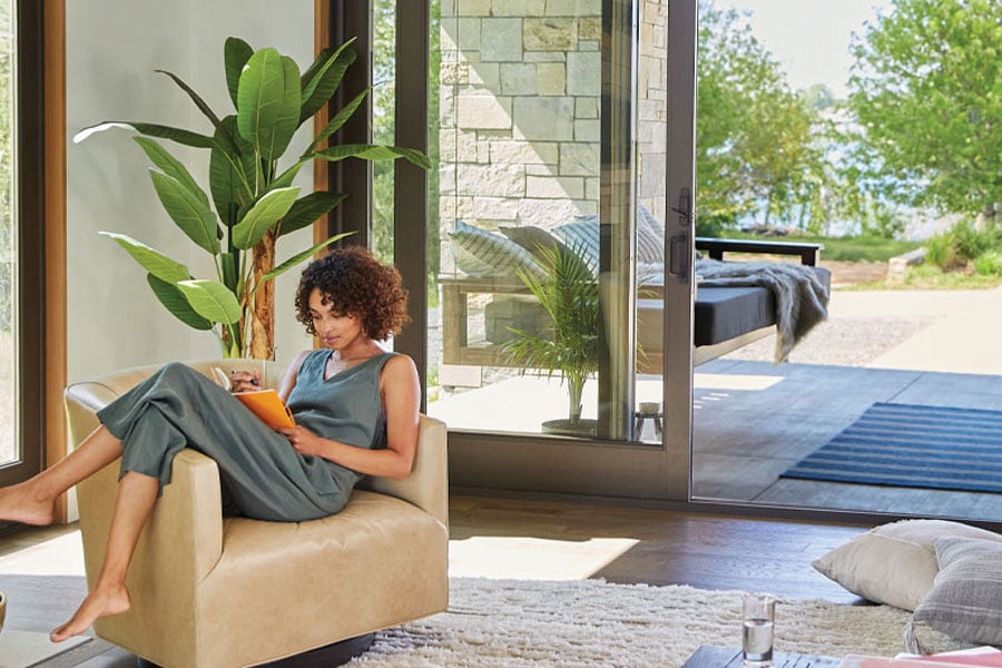 woman sitting on couch in living area with andersen doors going out to back patio area