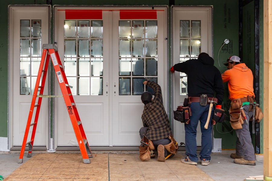 Three men installing a two-panel front door with sidelights on a home with Zip System WRB.