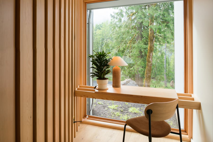 A desk that floats in front of a monumental picture window that begins at the floor and affords views of the forest outside.