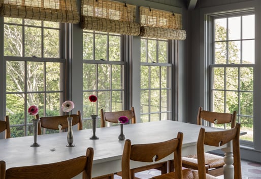 A dusty blue sunroom with tiled floors and tall double-hung windows overlooking a rolling green lawn. 