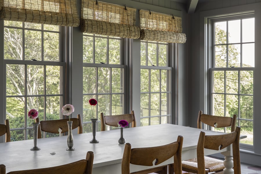 A dusty blue sunroom with tiled floors and tall double-hung windows overlooking a rolling green lawn. 