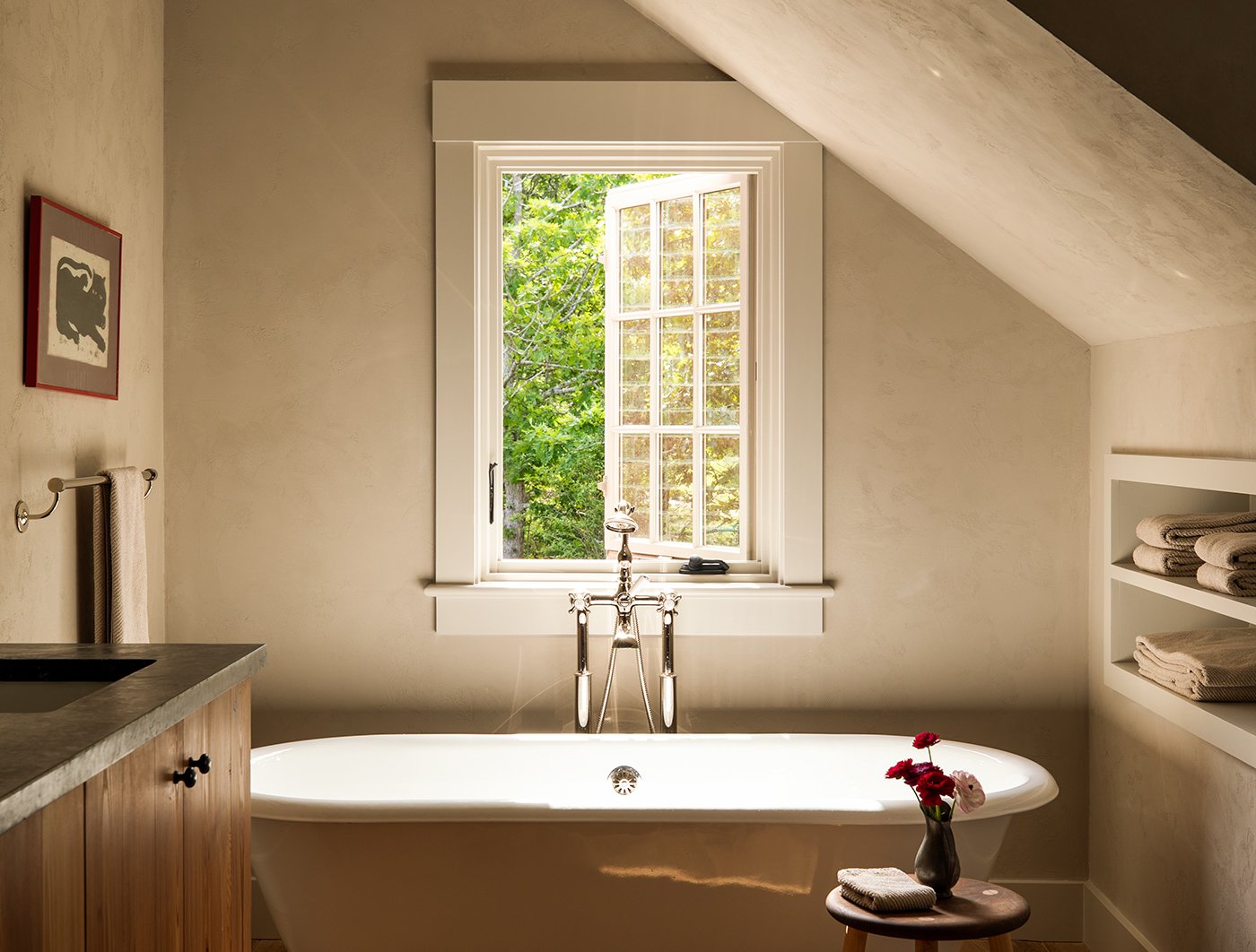 A moody bathroom with a soaking tub and, above it, a single Andersen® A-Series Casement Window with a white frame and 3-over-3 colonial grille pattern.