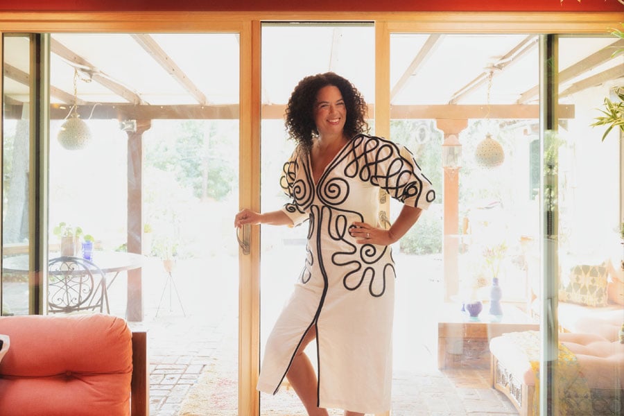 Justina Blakeney stands in front of the E-Series Gliding Patio Door on her lanai, on the left, and an exterior shot showing an outdoor seating area with couch, coffee table, footstool, and potted plants, on the right.