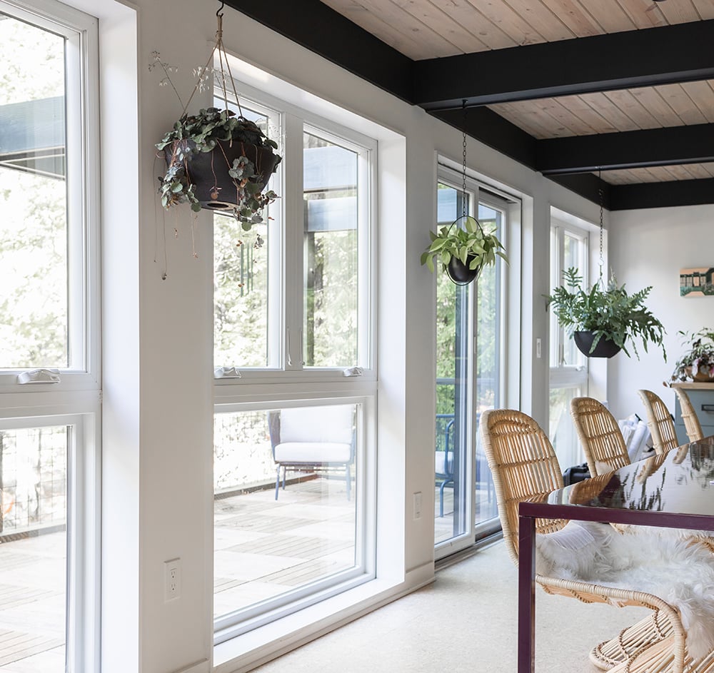 A wall with casement and picture windows and a gliding patio door with white interiors, wicker chairs and hanging plants.  