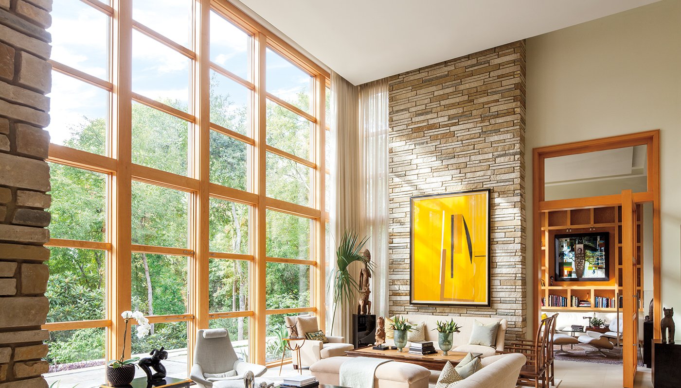 Floor- to- ceiling windows with light wood frames in a living room with tall ceilings and beige furniture.