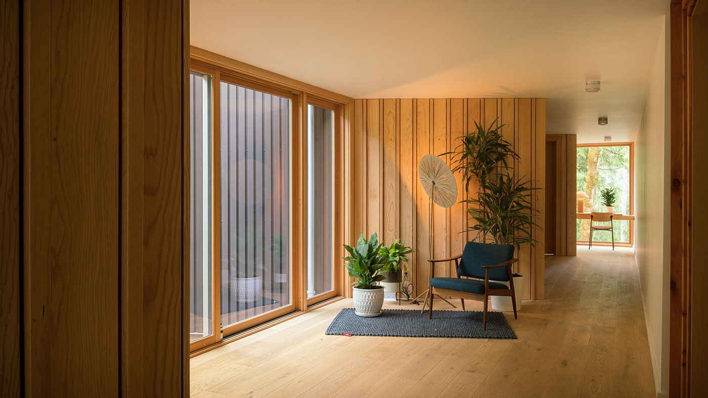 A wood-paneled hallway is well-lit thanks to an E-Series Gliding Patio Door along one side and a floor-to-ceiling E-Series Picture Window at the end.