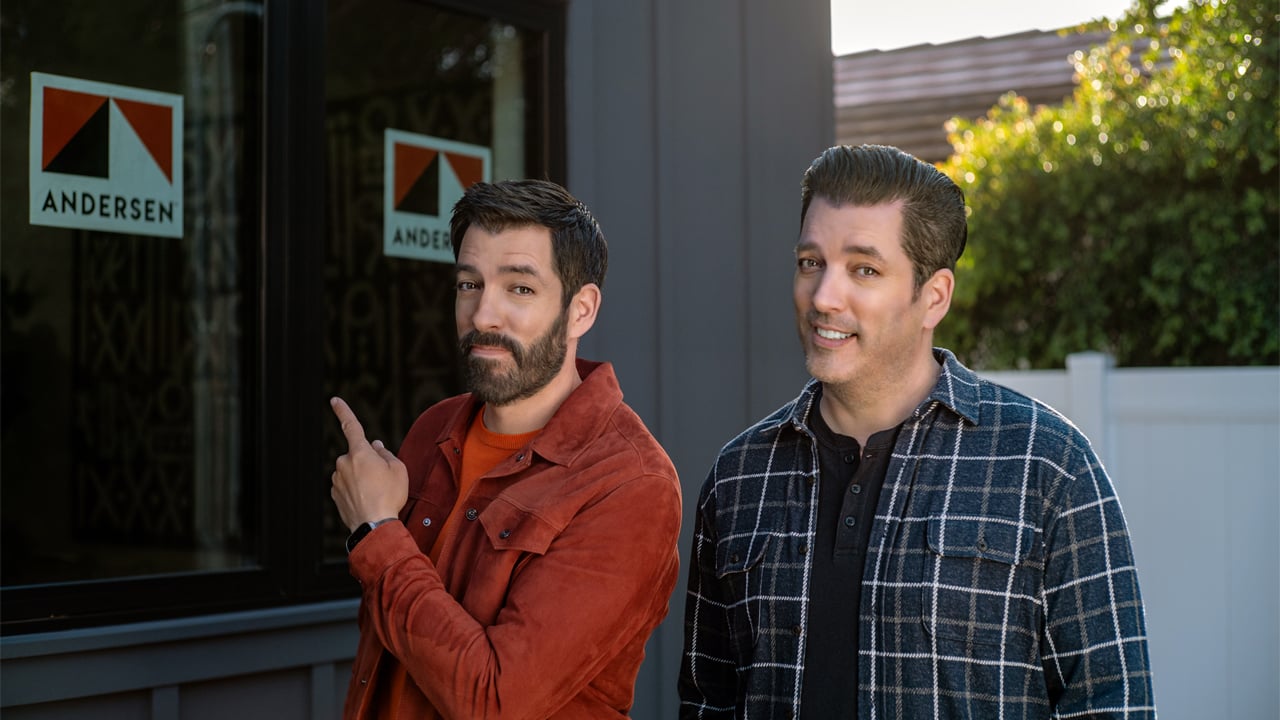 Drew and Jonathan Scott standing in front of new home with Andersen Windows stickers on the windows
