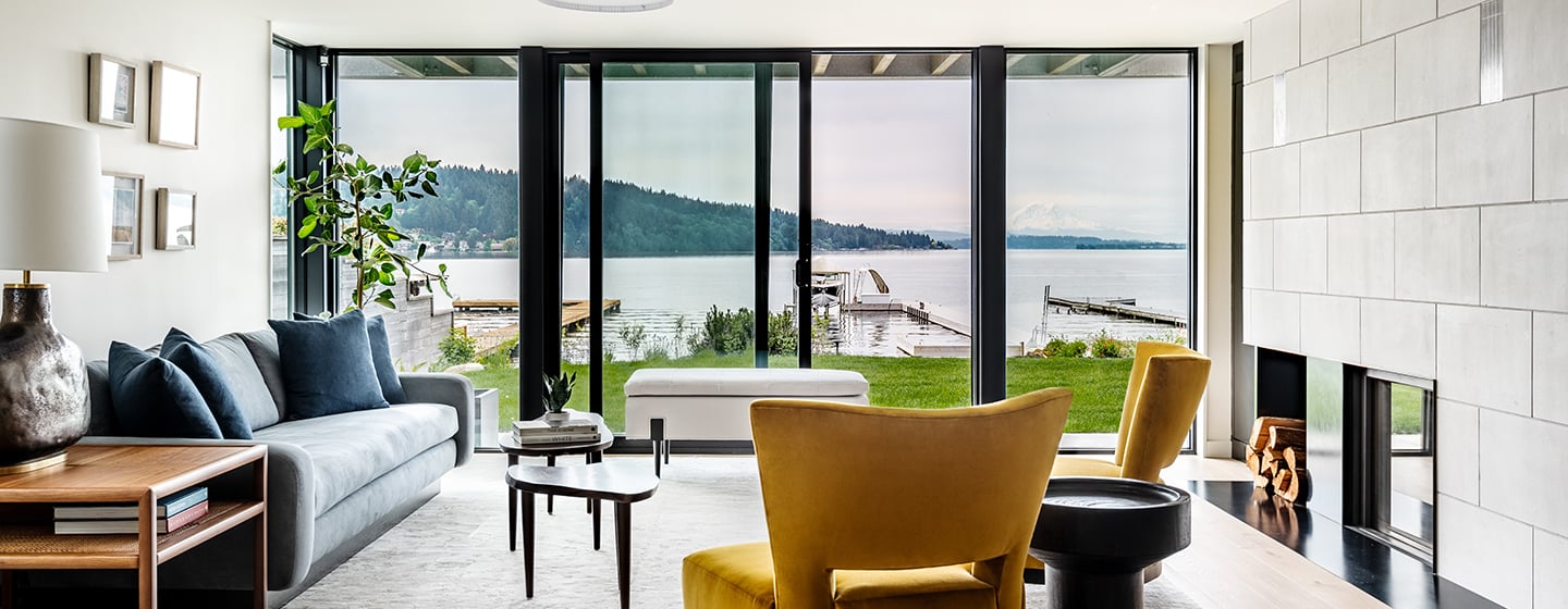 A living room with a wall of glass created by an Andersen® E-Series Gliding Patio Door flanked by stationary panels that wrap around a corner.