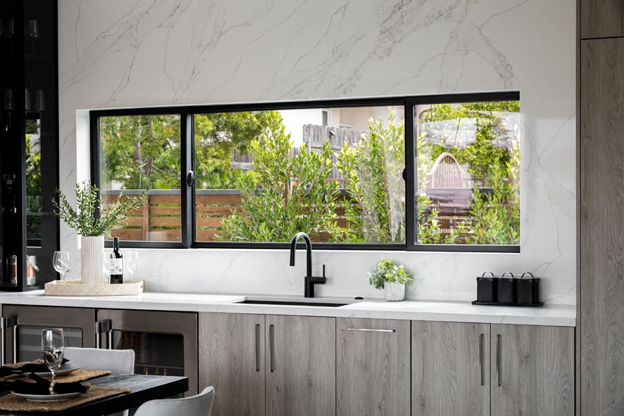 A kitchen with an extra-wide Andersen® 100 Series Gliding Window installed into a marble backsplash above the sink.