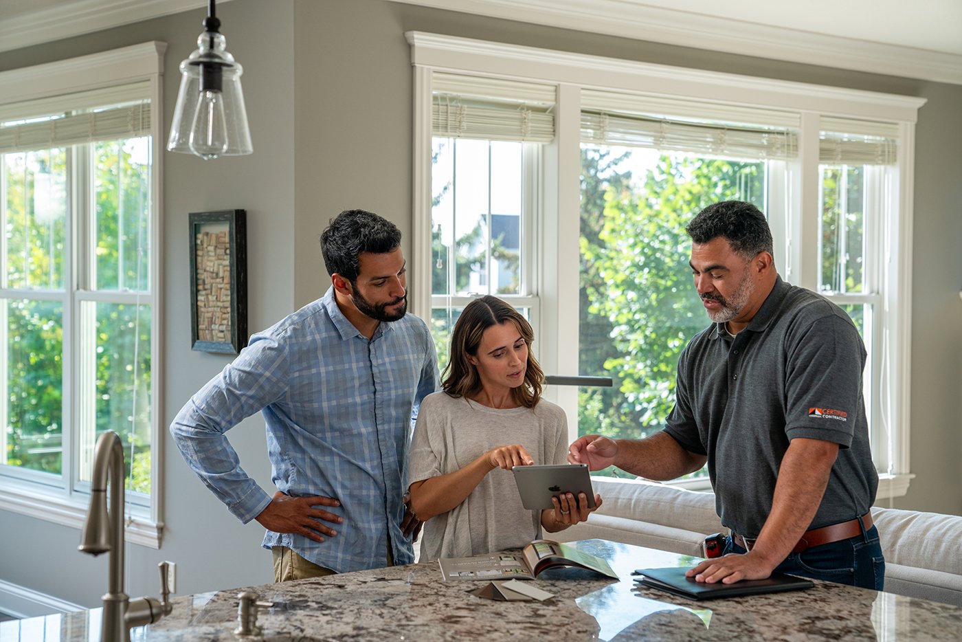 A couple looks at a tablet while having a discussion with a contractor in their kitchen.